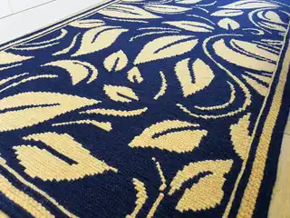 Hands embroidering a wool rug on a jute base using the Arraiolo technique
