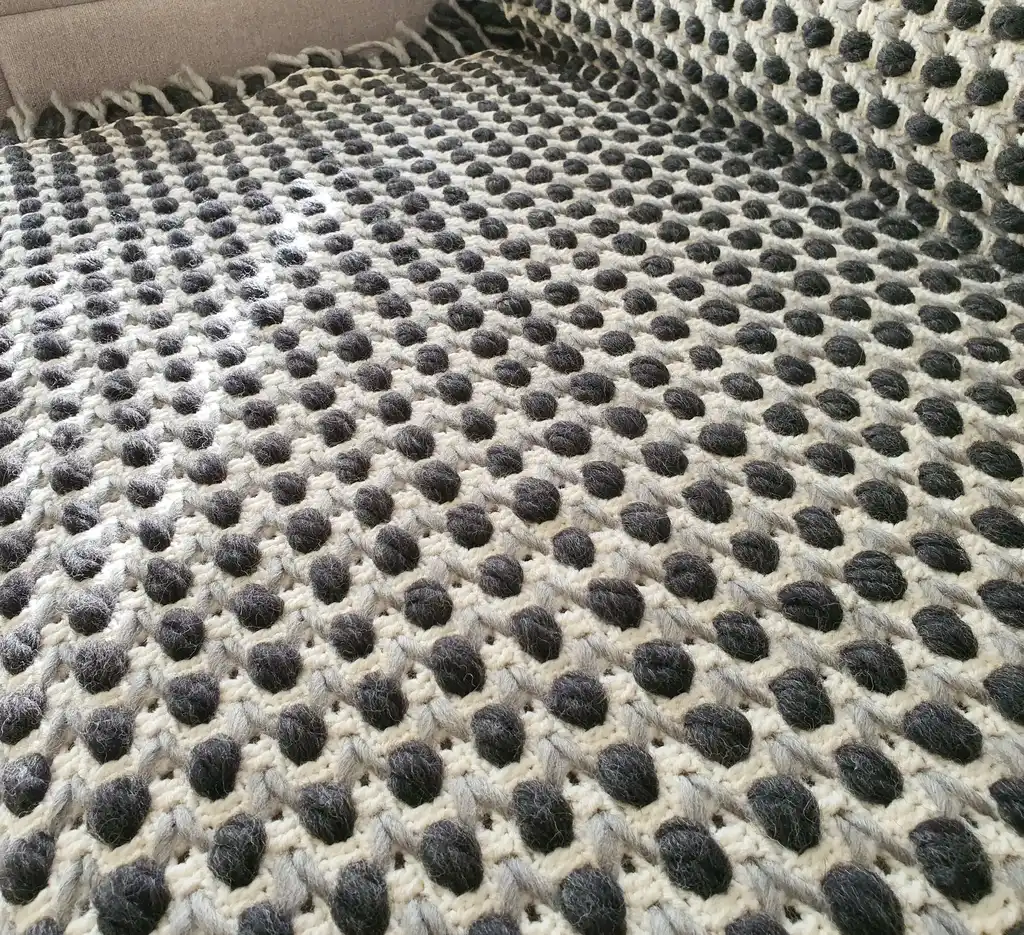Handmade crochet blanket in chunky merino wool with textured pattern.
