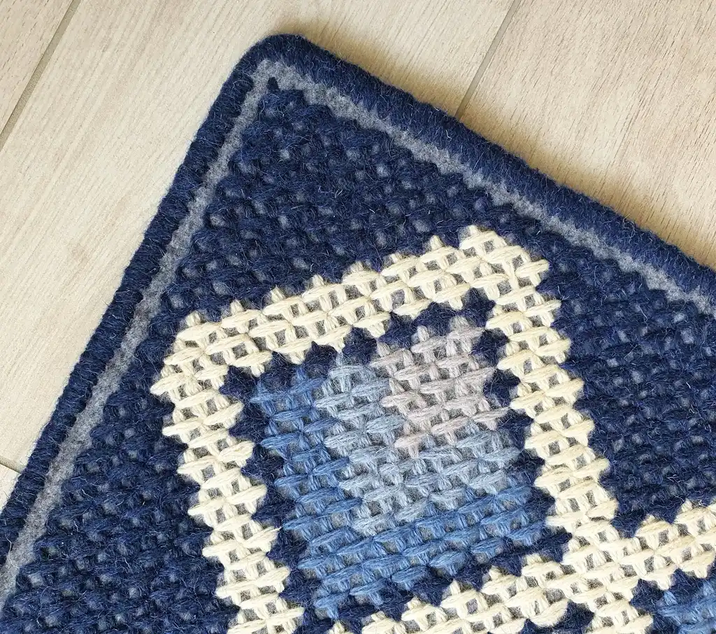 handcrafted cross-stitch wool rug on felt base with traditional patterns.