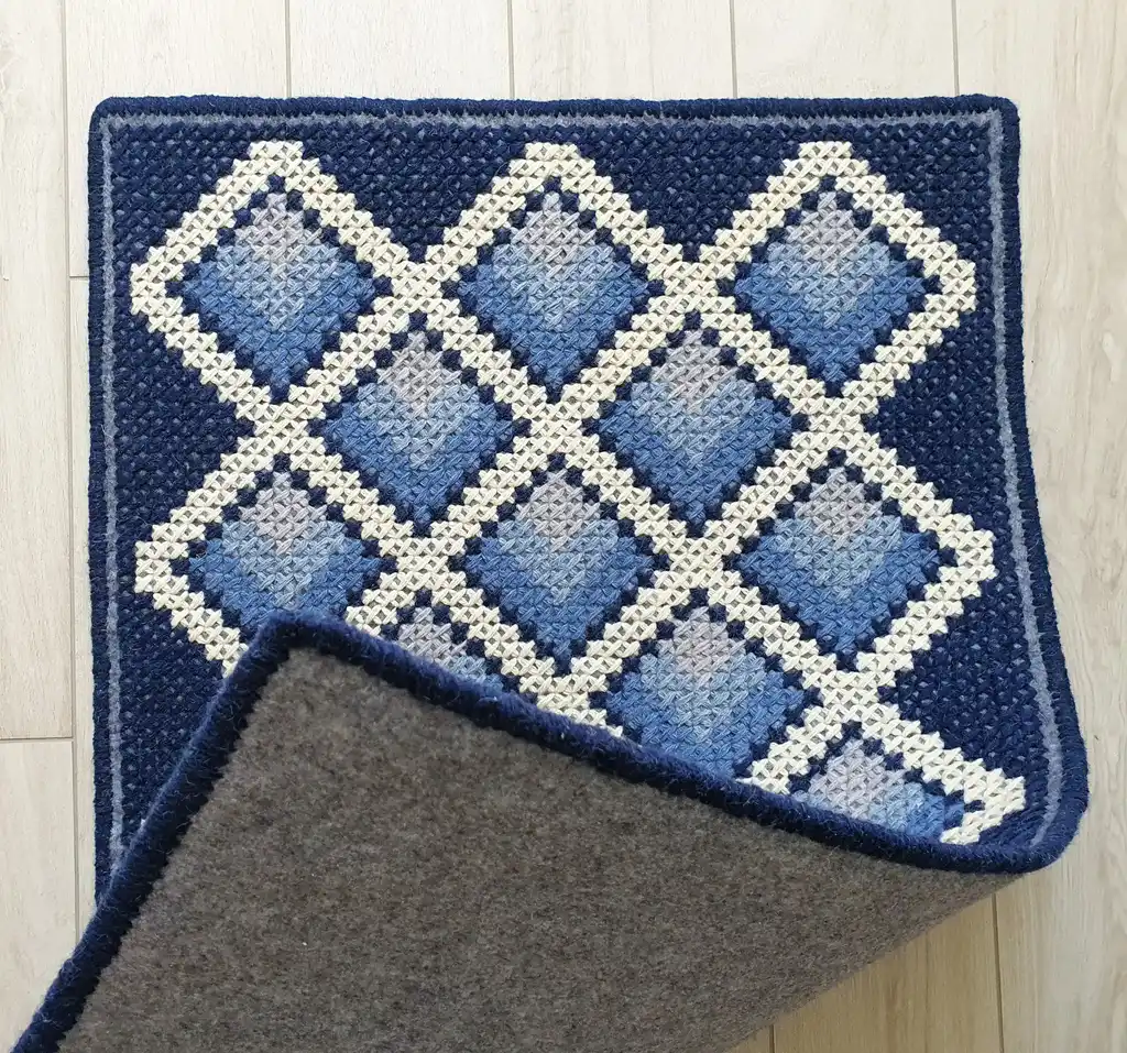 handcrafted cross-stitch wool rug on felt base with traditional patterns.