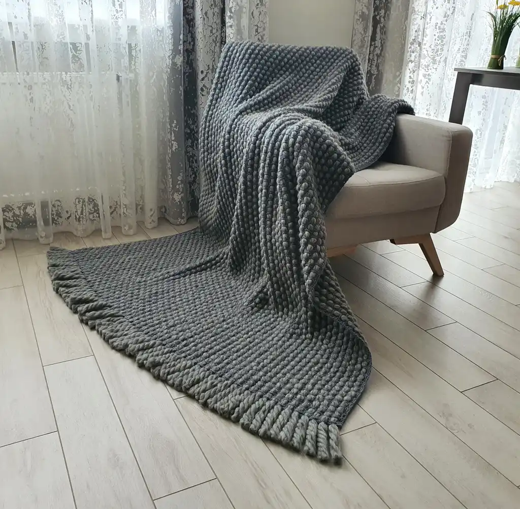 Handmade chunky wool crochet blanket in beige color, showcasing textured pattern and cozy appearance.