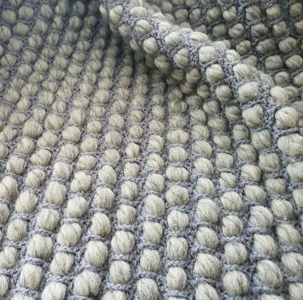 Handmade chunky wool crochet blanket in beige color, showcasing textured pattern and cozy appearance.