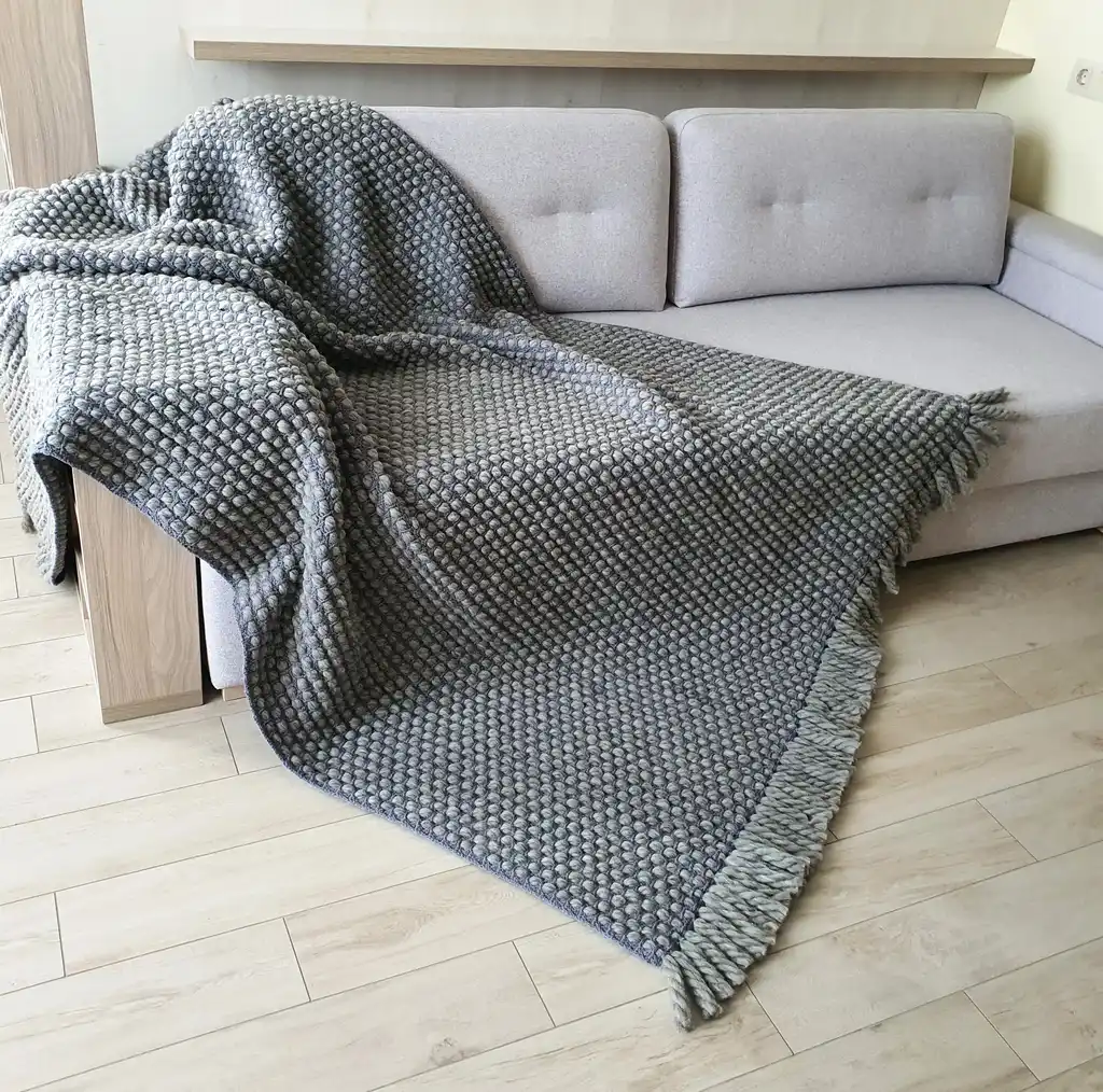 Handmade chunky wool crochet blanket in beige color, showcasing textured pattern and cozy appearance.