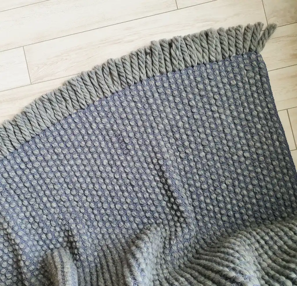 Handmade chunky wool crochet blanket in beige color, showcasing textured pattern and cozy appearance.