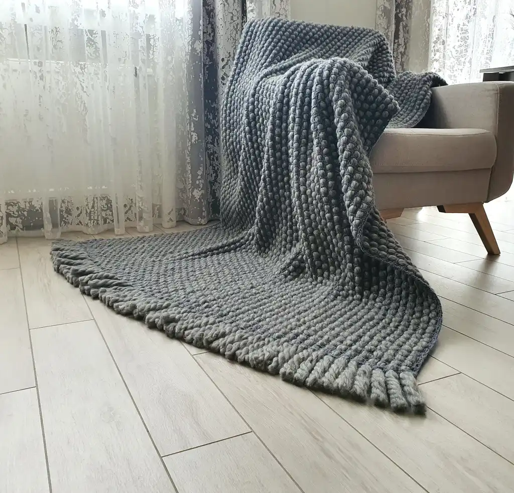Handmade chunky wool crochet blanket in beige color, showcasing textured pattern and cozy appearance.