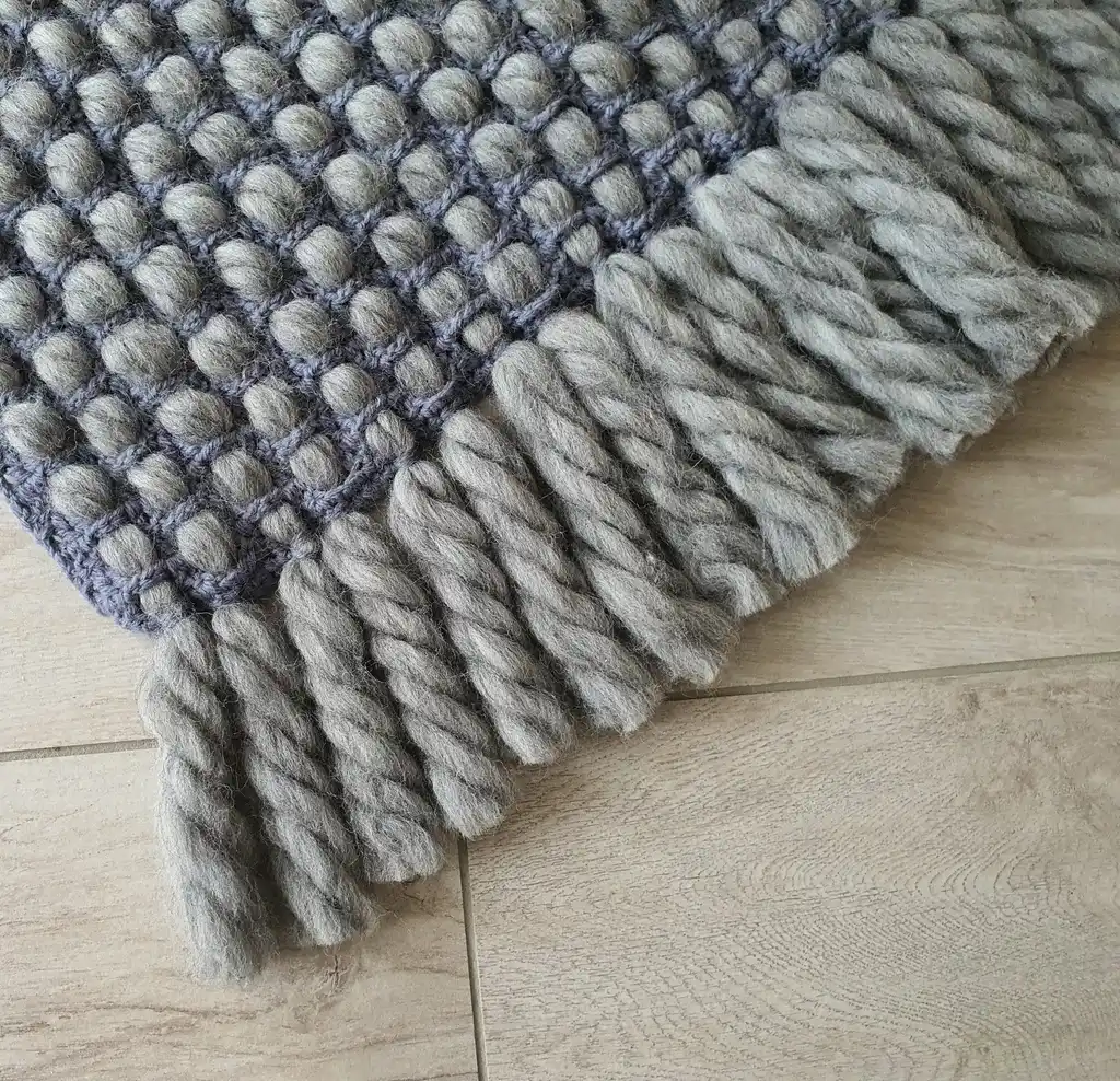 Handmade chunky wool crochet blanket in beige color, showcasing textured pattern and cozy appearance.