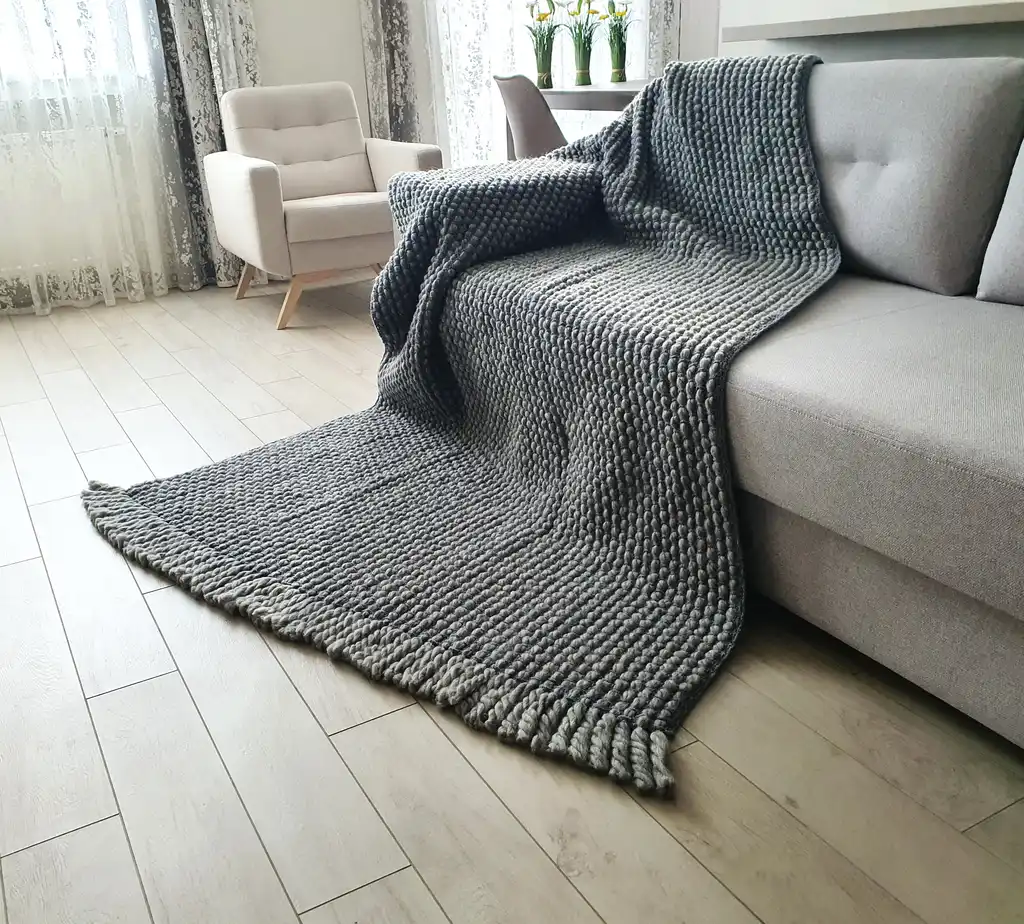 Handmade chunky wool crochet blanket in beige color, showcasing textured pattern and cozy appearance.