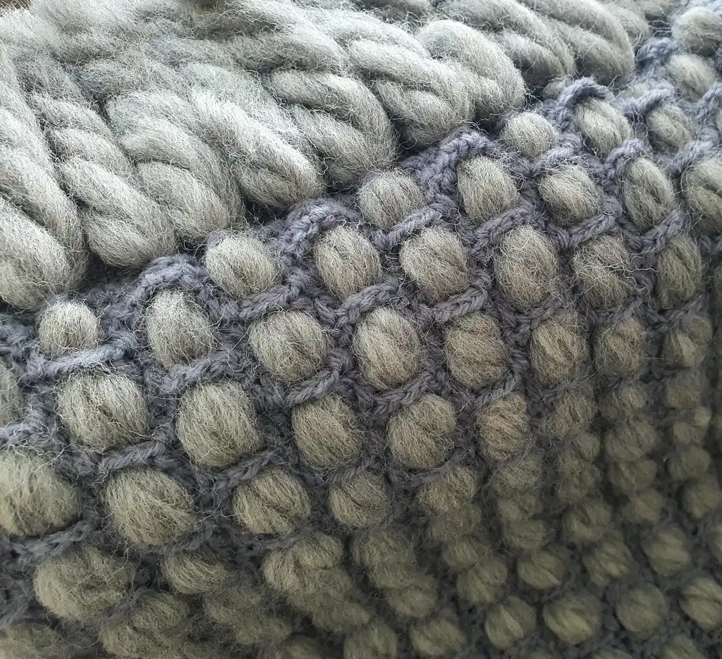 Handmade chunky wool crochet blanket in beige color, showcasing textured pattern and cozy appearance.