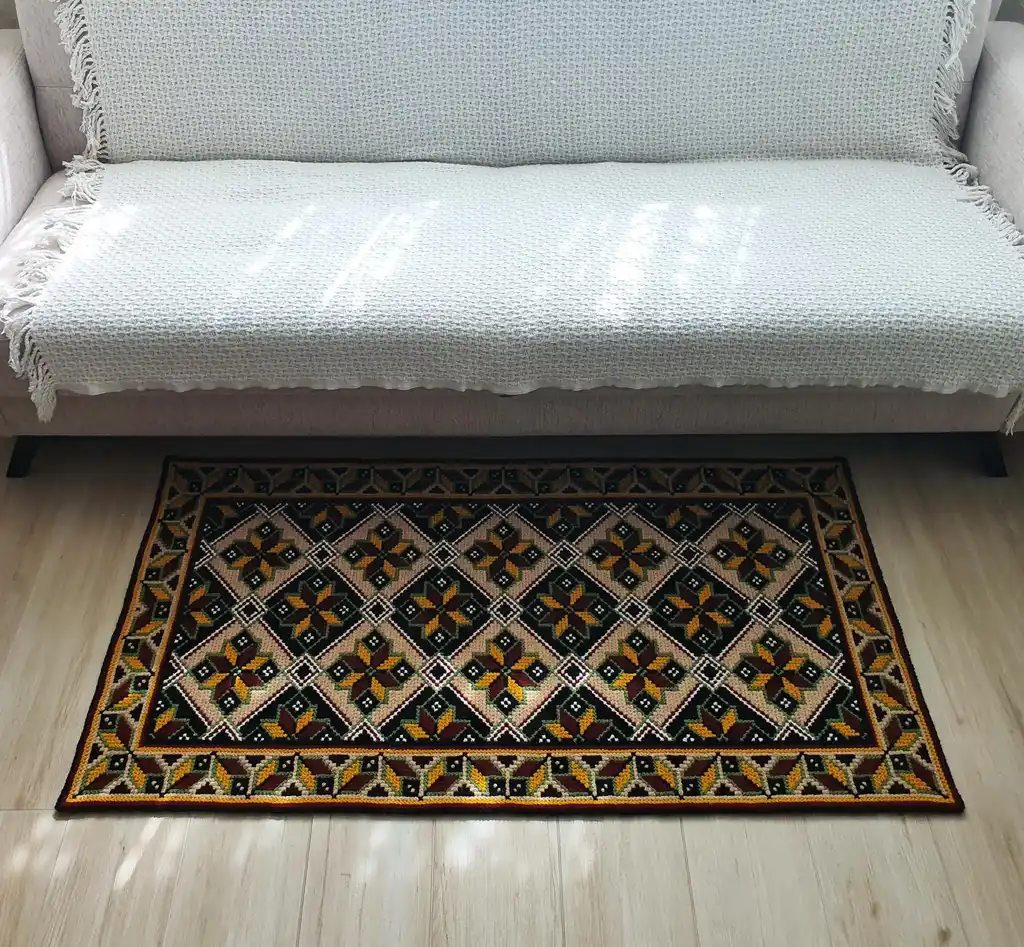 Handmade cross-stitch wool rug with traditional needlework patterns.