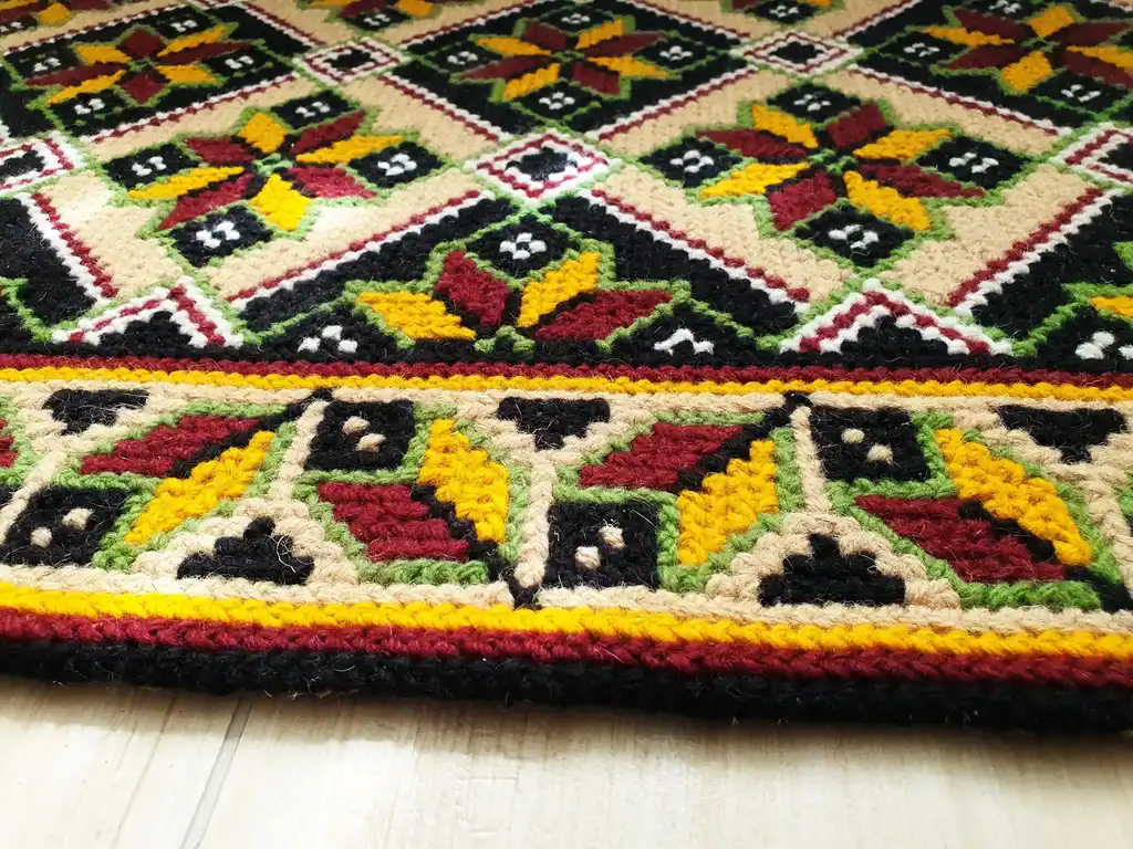 Handmade cross-stitch wool rug with traditional needlework patterns.
