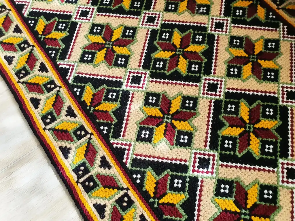 Handmade cross-stitch wool rug with traditional needlework patterns.