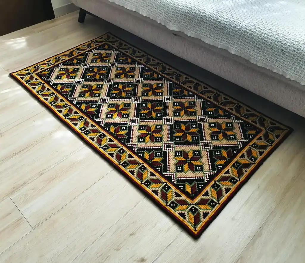 Handmade cross-stitch wool rug with traditional needlework patterns.
