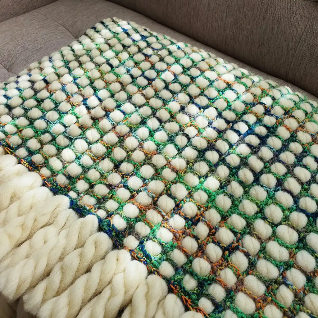 Luxurious chunky wool crochet blanket with intricate handmade patterns in neutral tones.