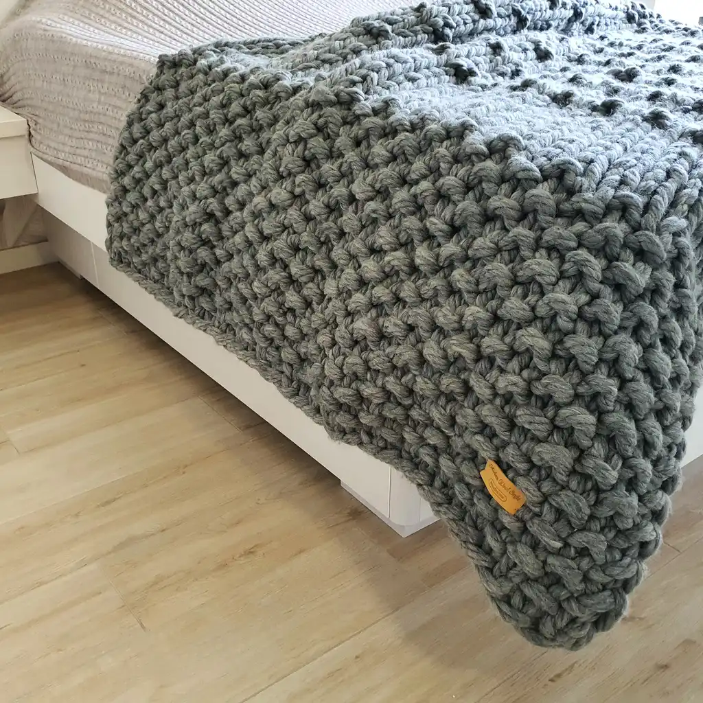 Chunky wool knitted blanket in neutral color with textured pattern, displayed on modern furniture.