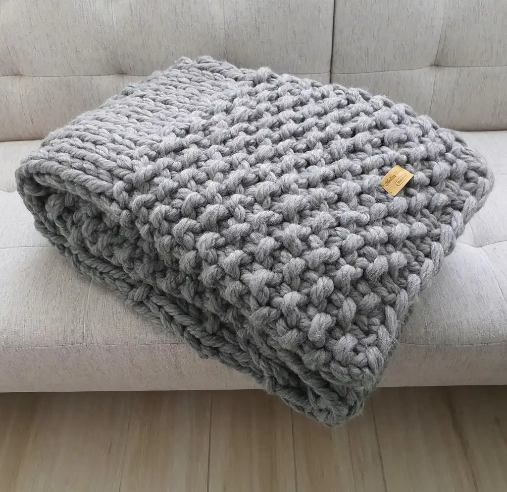 Chunky wool knitted blanket in neutral color with textured pattern, displayed on modern furniture.