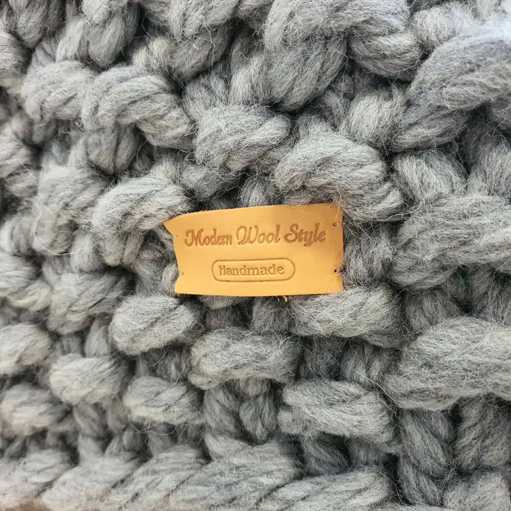 Chunky wool knitted blanket in neutral color with textured pattern, displayed on modern furniture.