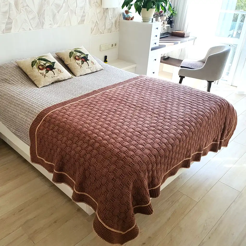 Handmade chunky knitted throw in terracotta color with beige border, textured pattern.