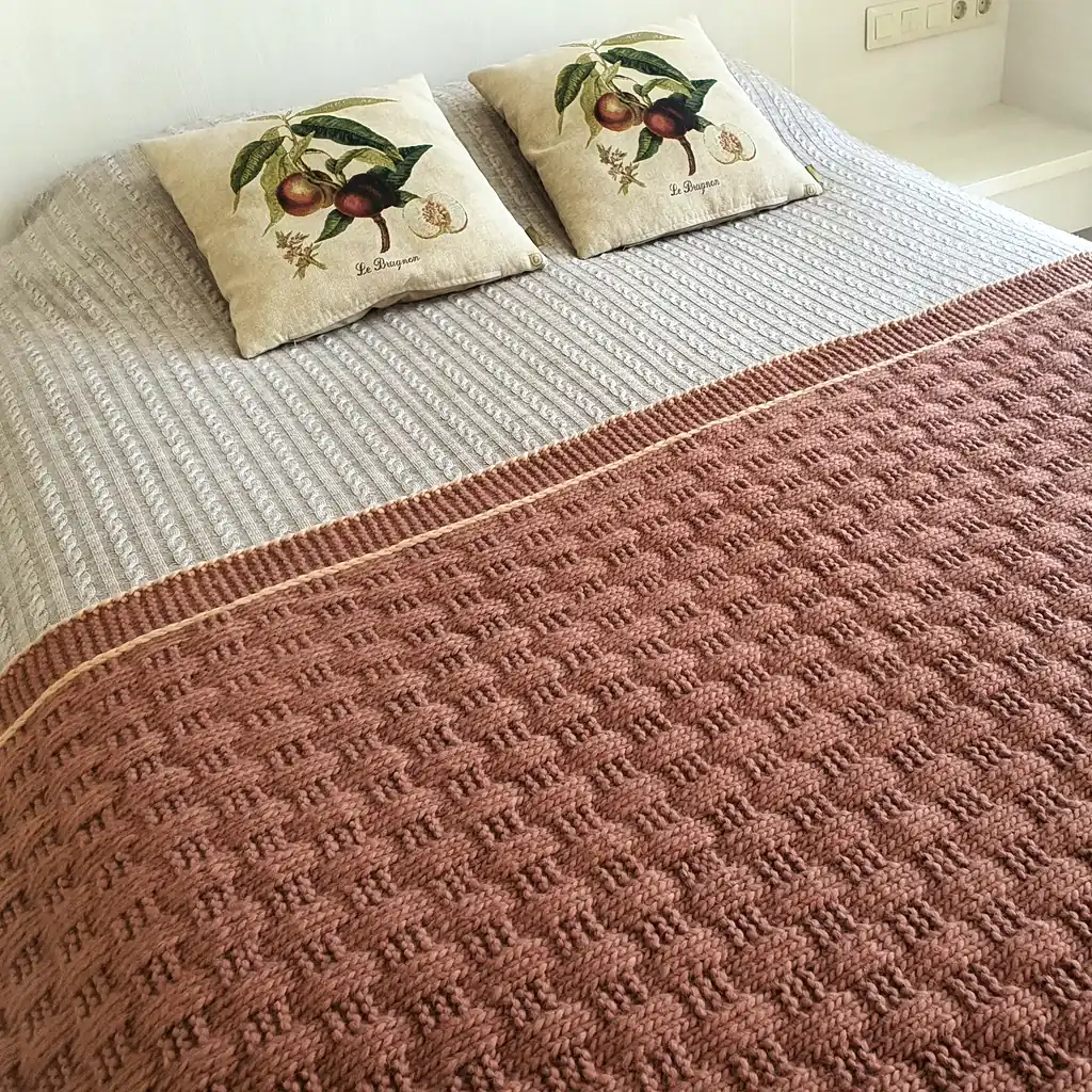 Handmade chunky knitted throw in terracotta color with beige border, textured pattern.