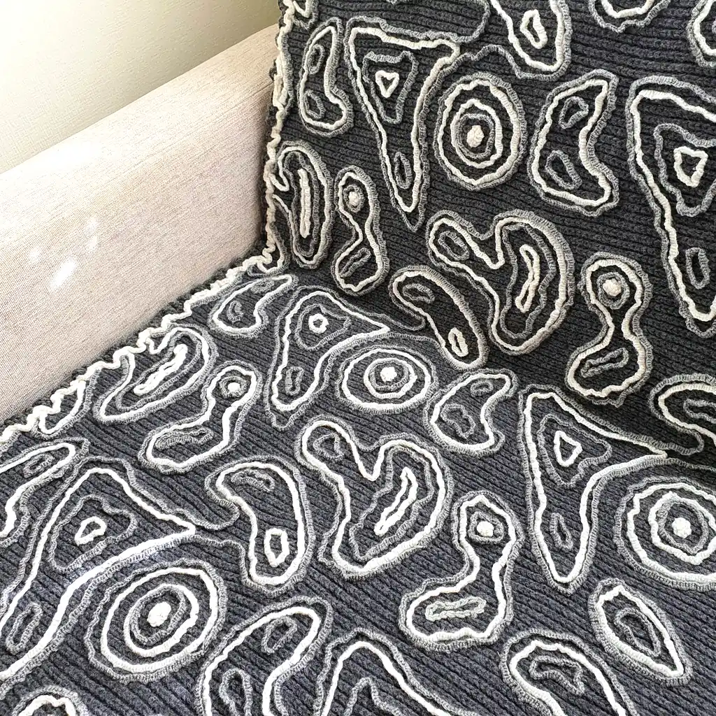 Gray wool blanket with voluminous decorative crochet elements and abstract pattern.
