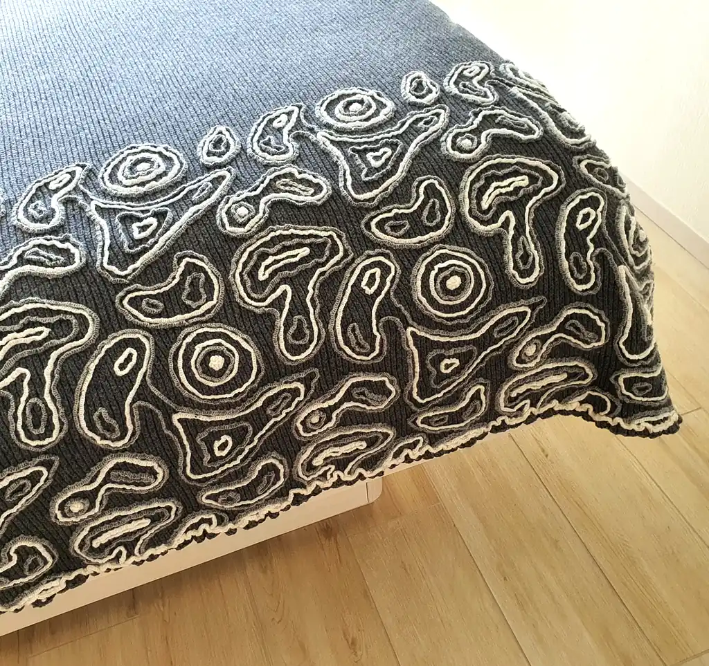 Gray wool blanket with voluminous decorative crochet elements and abstract pattern.