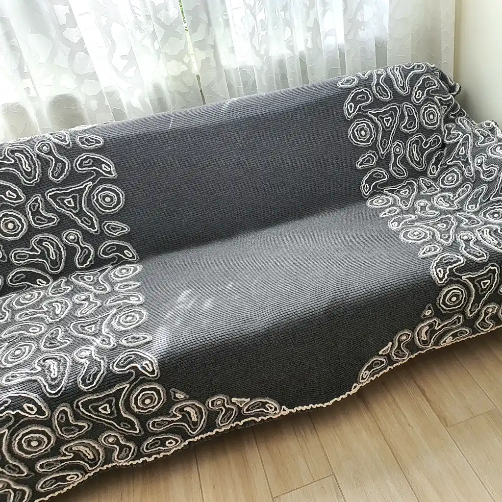 Gray wool blanket with voluminous decorative crochet elements and abstract pattern.