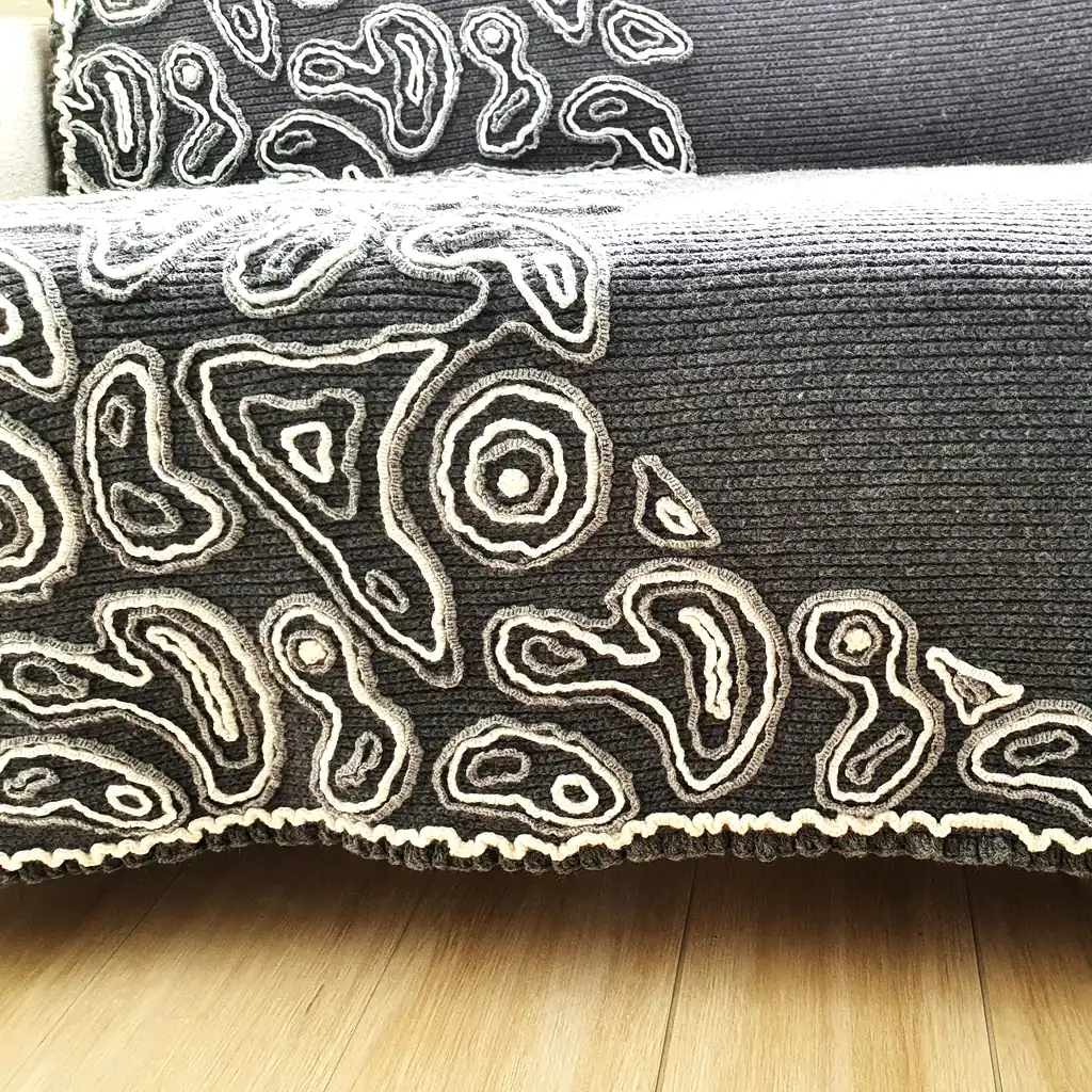 Gray wool blanket with voluminous decorative crochet elements and abstract pattern.