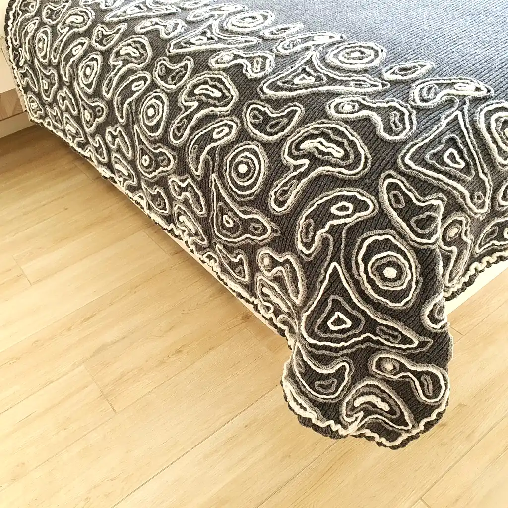Gray wool blanket with voluminous decorative crochet elements and abstract pattern.