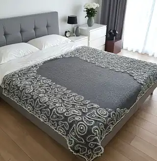Gray wool blanket with voluminous decorative crochet elements and abstract pattern.