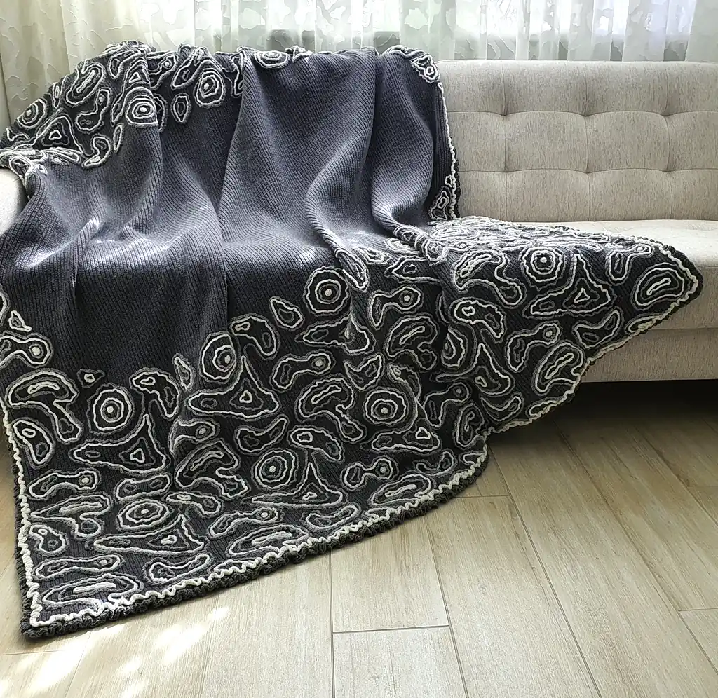 Gray wool blanket with voluminous decorative crochet elements and abstract pattern.