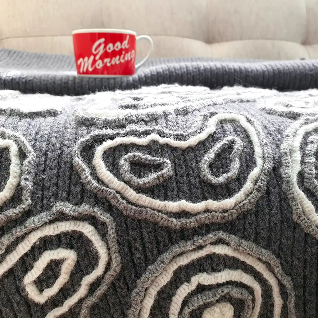 Gray wool blanket with voluminous decorative crochet elements and abstract pattern.
