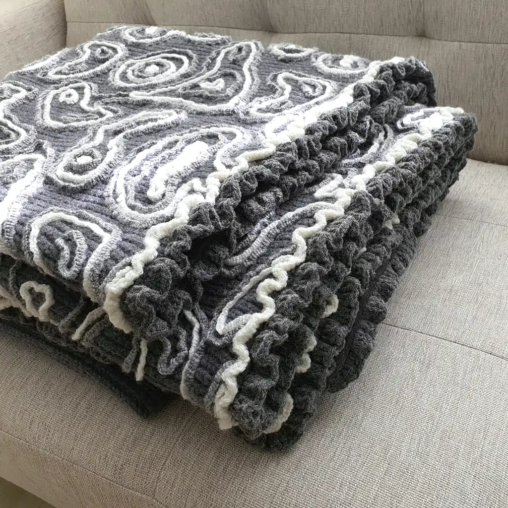 Gray wool blanket with voluminous decorative crochet elements and abstract pattern.