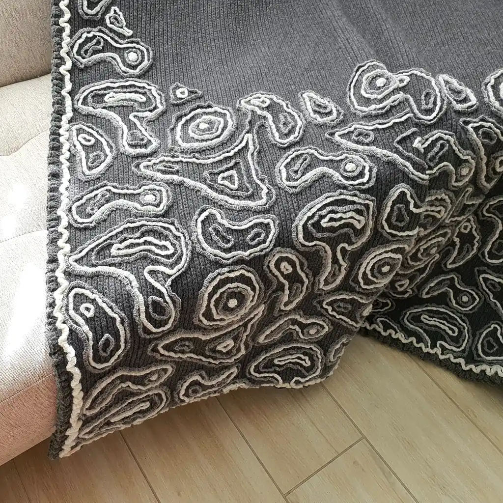 Gray wool blanket with voluminous decorative crochet elements and abstract pattern.