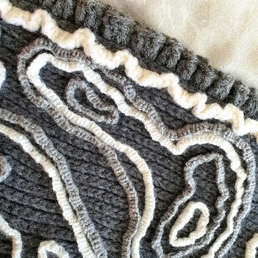Gray wool blanket with voluminous decorative crochet elements and abstract pattern.