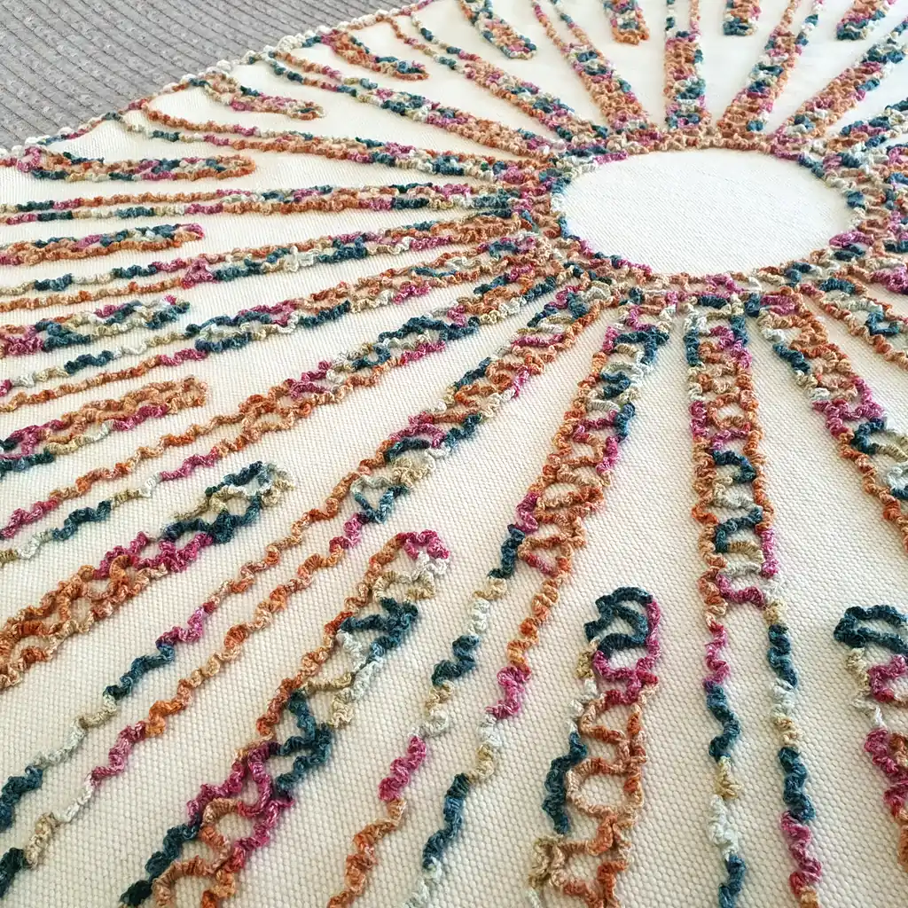 Close-up of textured embroidery in orange, green, and pink on soft cream wool fabric.