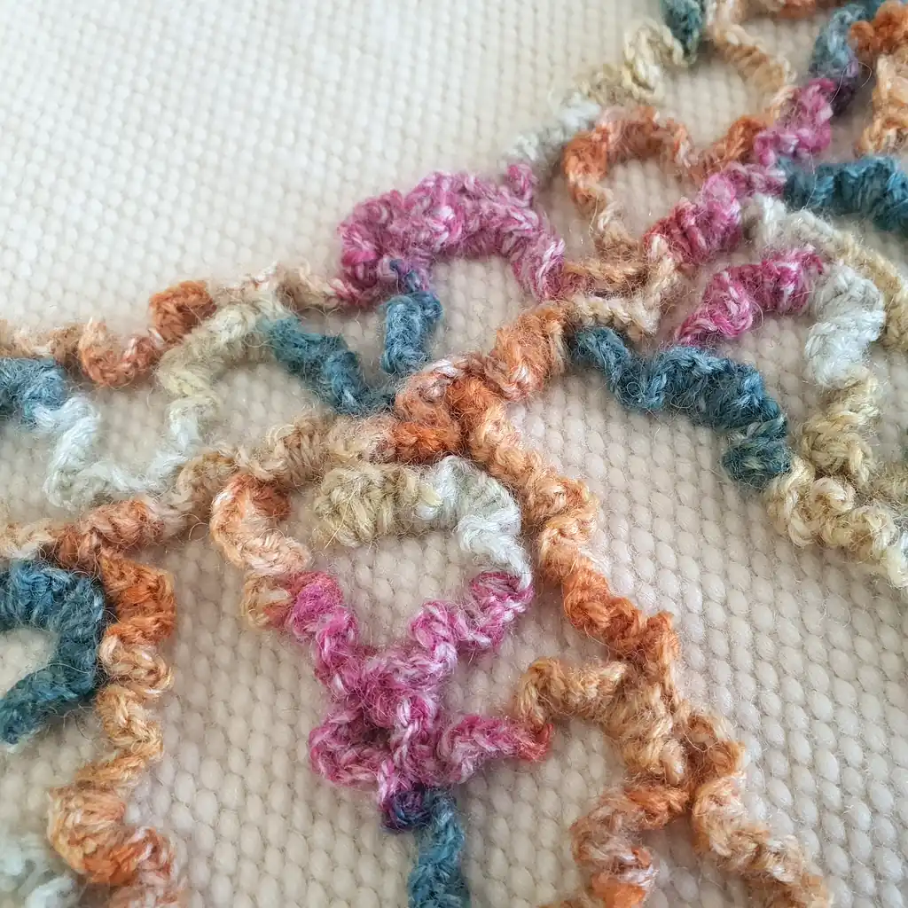 Detail of artisan embroidery with 3D wool texture on natural woven base.