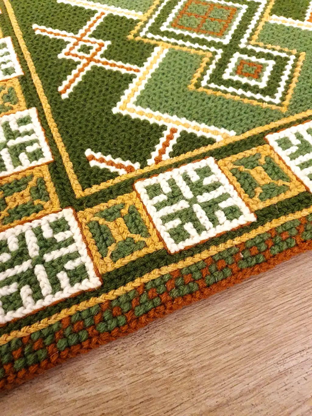 Handmade wool runner rug with authentic Ukrainian ethnic ornament, featuring green and earthy tones, lying on a light wood floor in a modern interior.