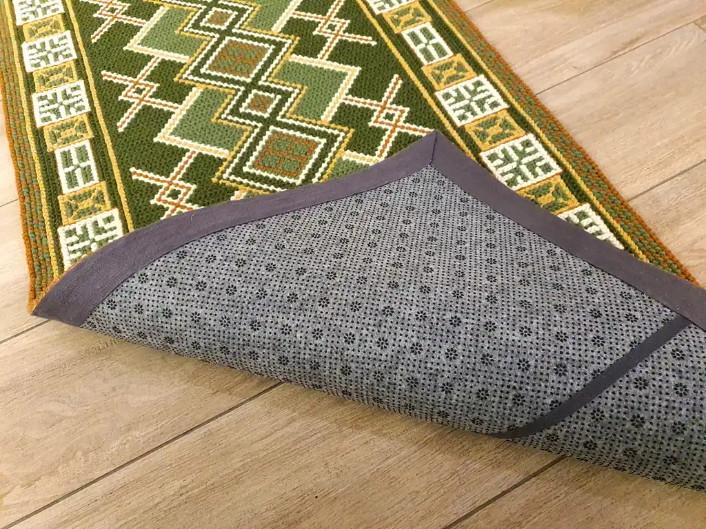 Handmade wool runner rug with authentic Ukrainian ethnic ornament, featuring green and earthy tones, lying on a light wood floor in a modern interior.