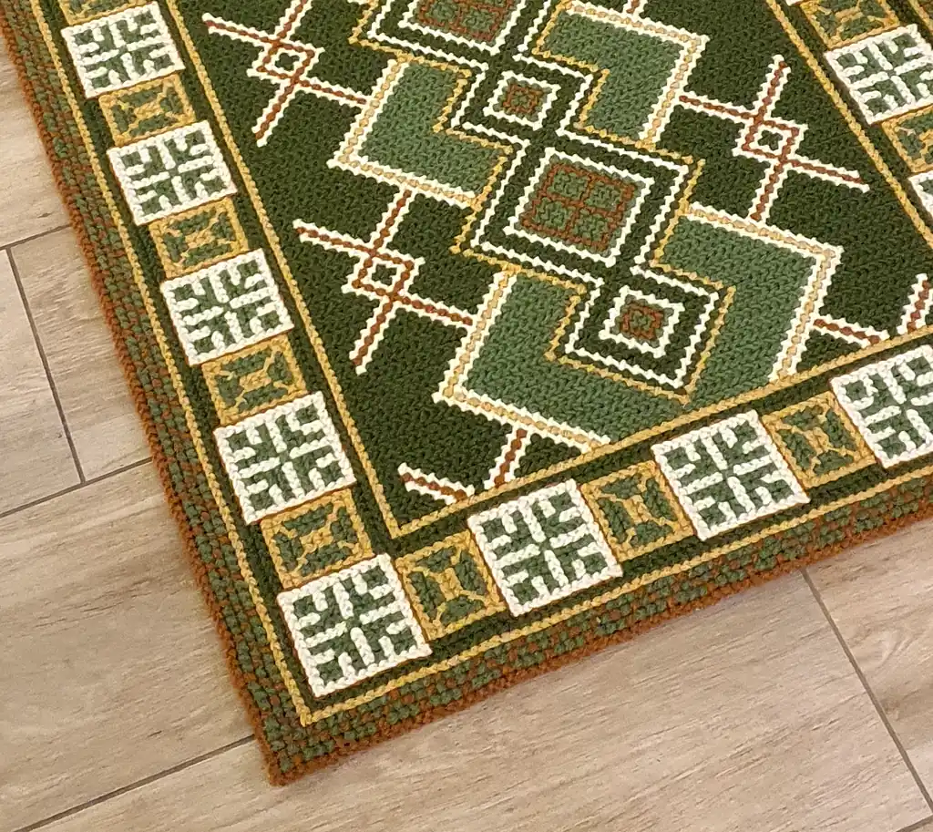 Handmade wool runner rug with authentic Ukrainian ethnic ornament, featuring green and earthy tones, lying on a light wood floor in a modern interior.