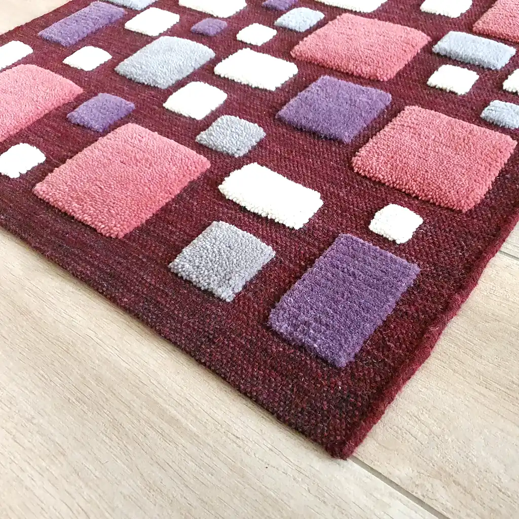 Close-up of textured hand-shorn wool elements on a hand-loomed burgundy base. Natural fiber rug detail showcasing premium, handcrafted quality and a soft, tactile surface.