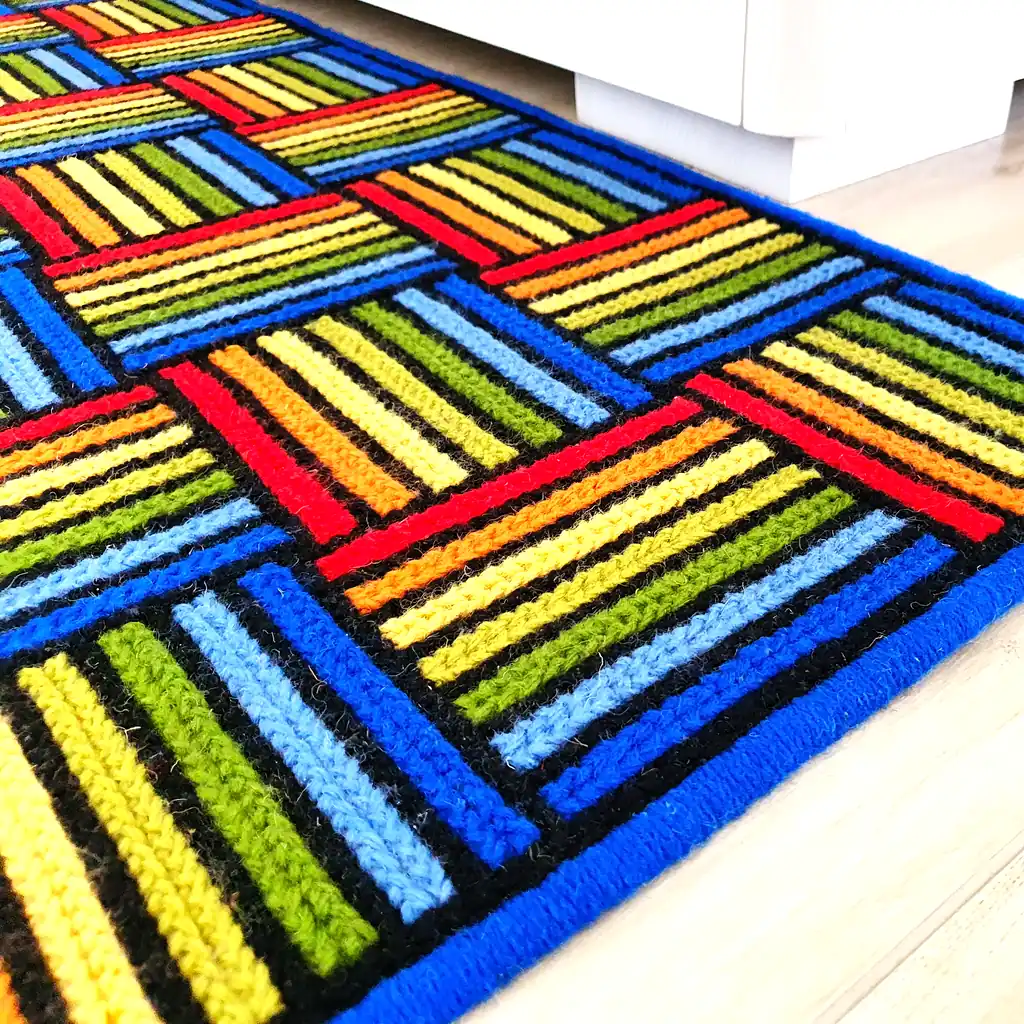 High-angle view of a rectangular handmade rug with a colorful rainbow basketweave pattern.
