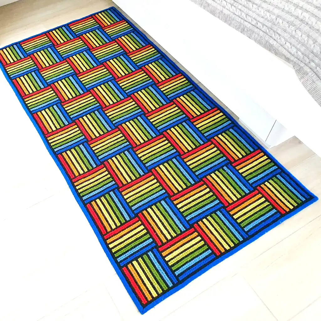 Brightly colored geometric rug placed next to a white modern bed on a light wood floor.