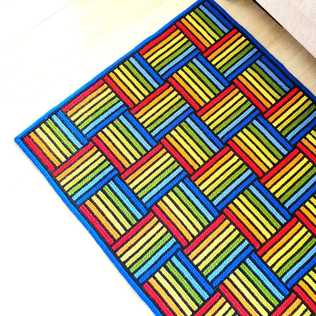 Brightly colored geometric rug placed next to a white modern bed on a light wood floor.