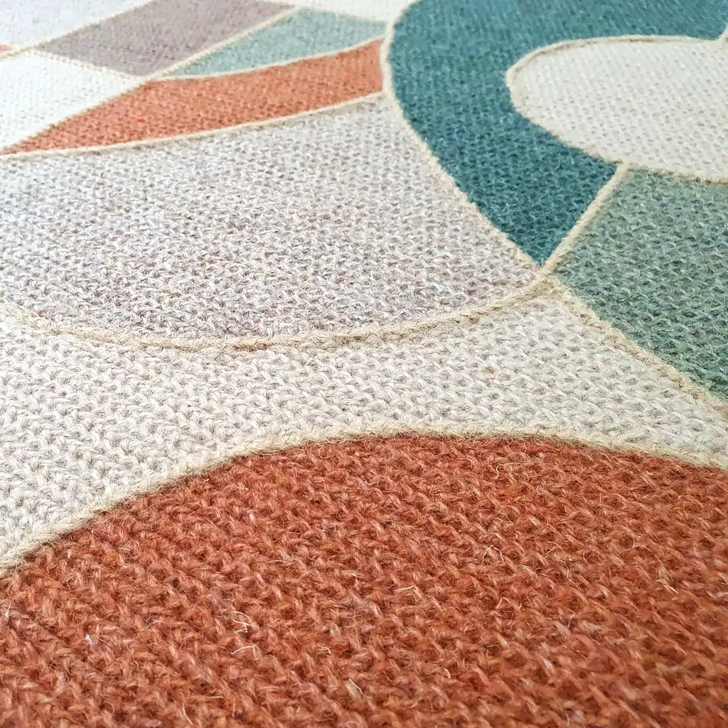Handmade embroidered wool rug with geometric mosaic pattern in teal, orange, and cream colors with thick plush lining and natural jute border