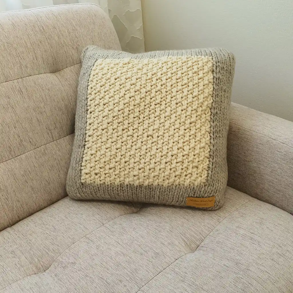 Handmade merino wool knitted cushion with textured pattern in gray and warm white colors.