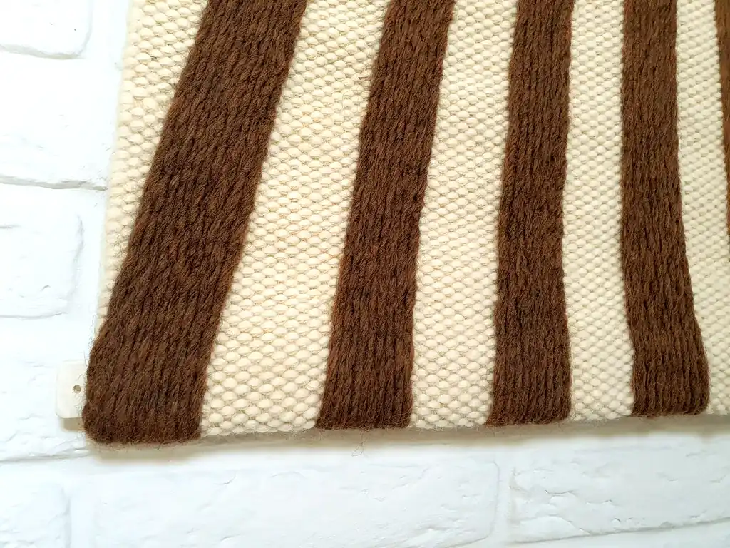 Handmade knitted wool wall hanging with radiating brown and beige fountain pattern creating optical depth effect