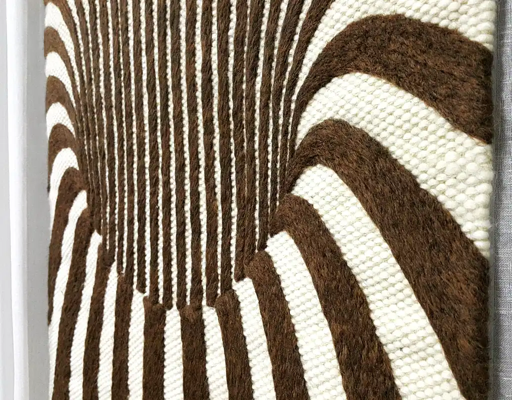 Handmade knitted wool wall hanging with radiating brown and beige fountain pattern creating optical depth effect