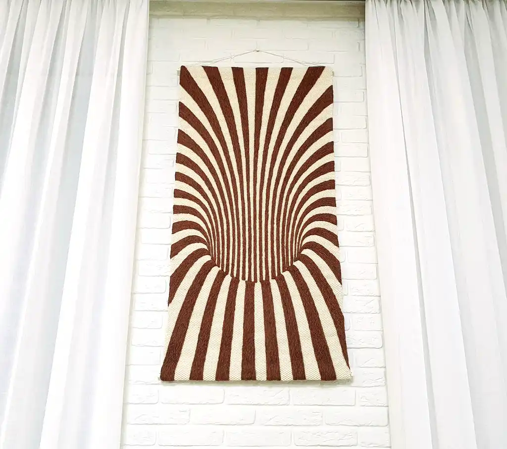 Handmade knitted wool wall hanging with radiating brown and beige fountain pattern creating optical depth effect