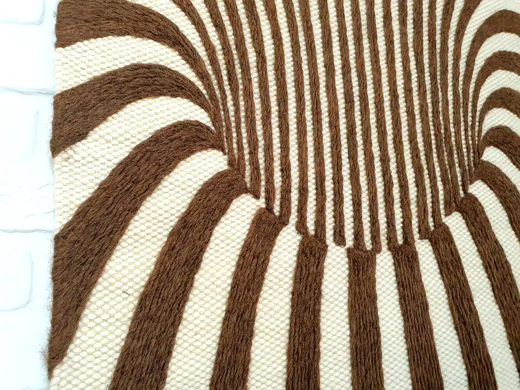 Handmade knitted wool wall hanging with radiating brown and beige fountain pattern creating optical depth effect