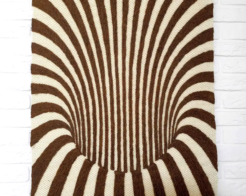 Handmade knitted wool wall hanging with radiating brown and beige fountain pattern creating optical depth effect